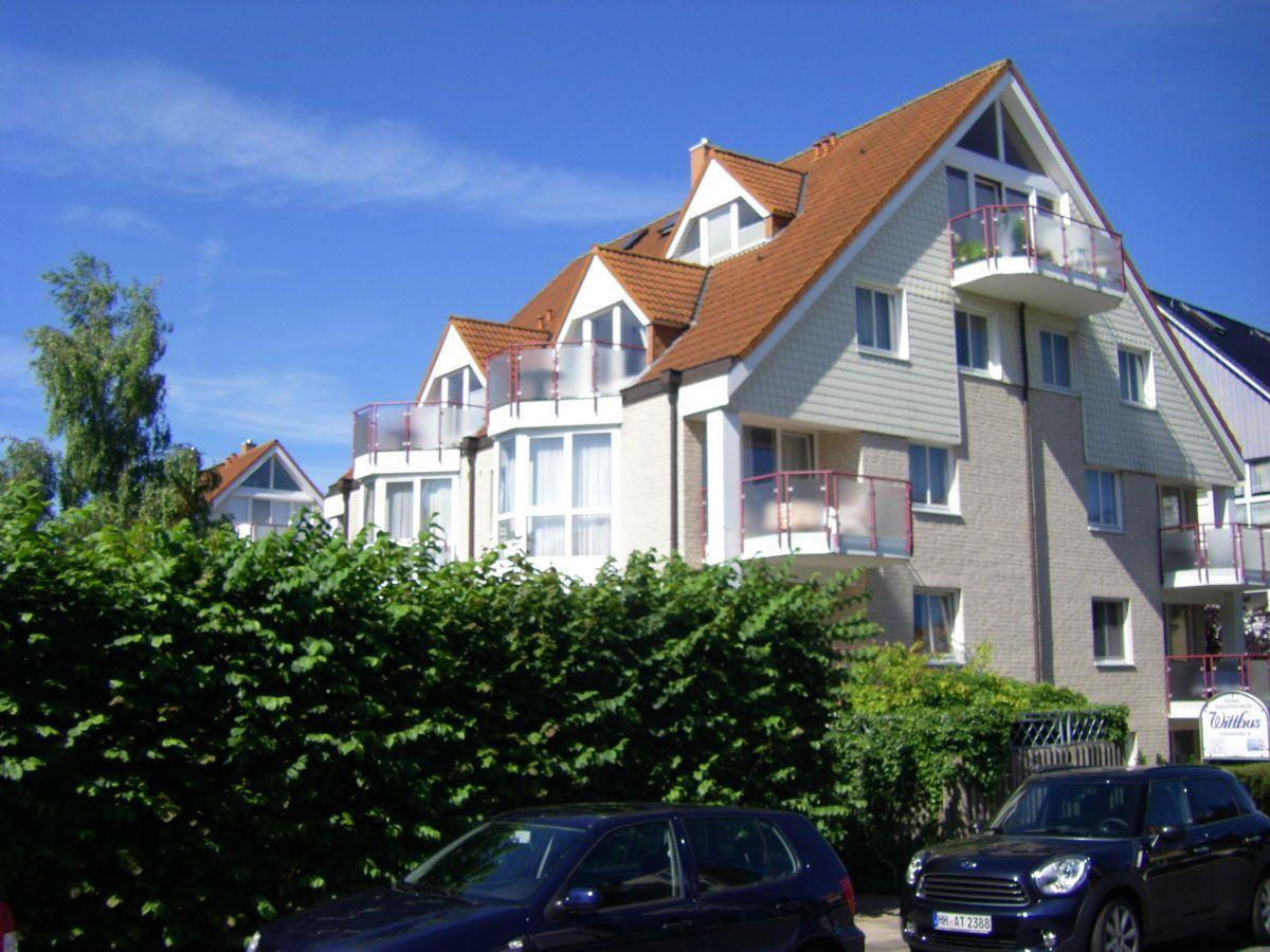 Mehrfamilienhaus mit Balkonen und rotem Dach unter blauem Himmel.