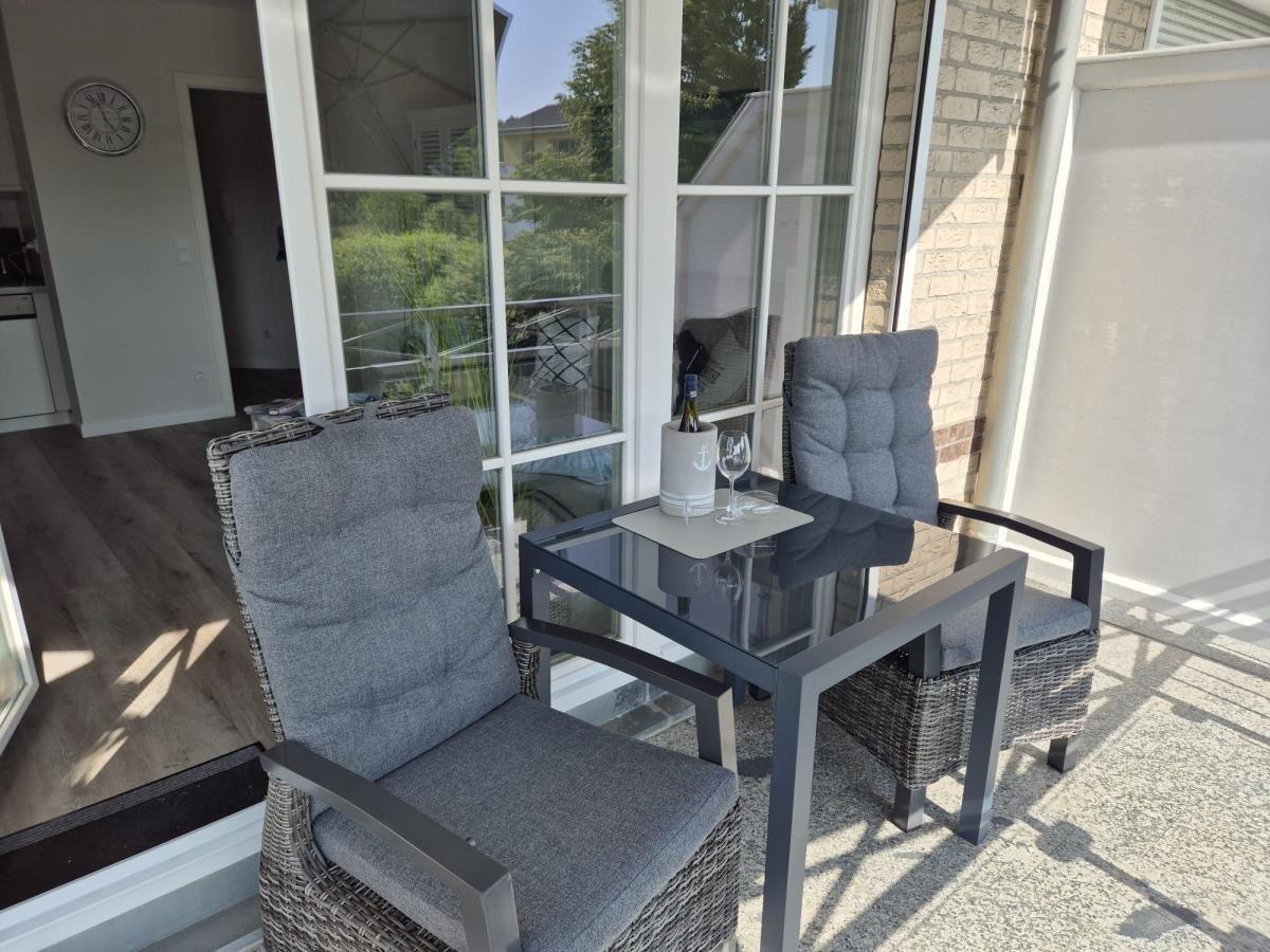 Terrasse mit zwei Stühlen und Tisch, daneben Glasfront und Garten.