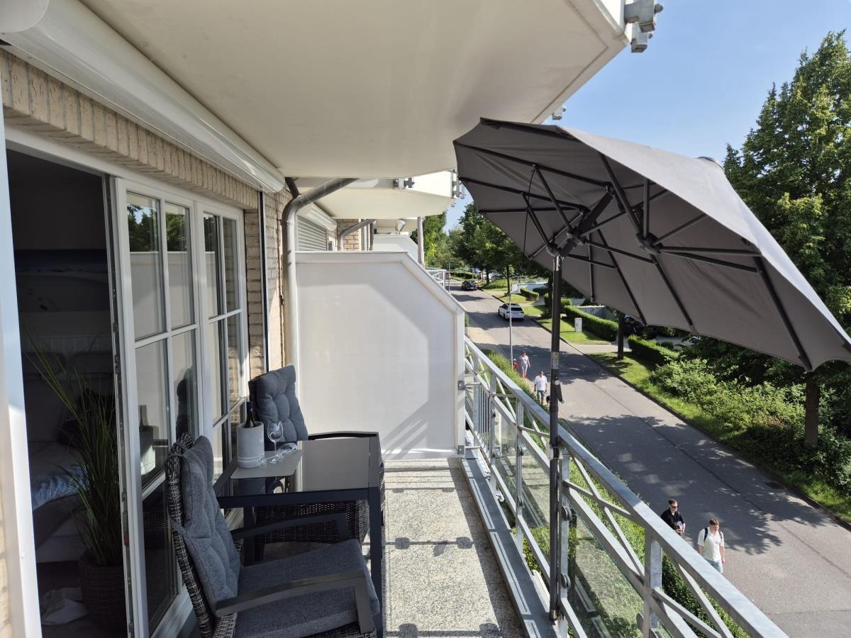 Terrasse mit Sitzgruppe, Sonnenschirm und Blick auf Straße mit Bäumen.