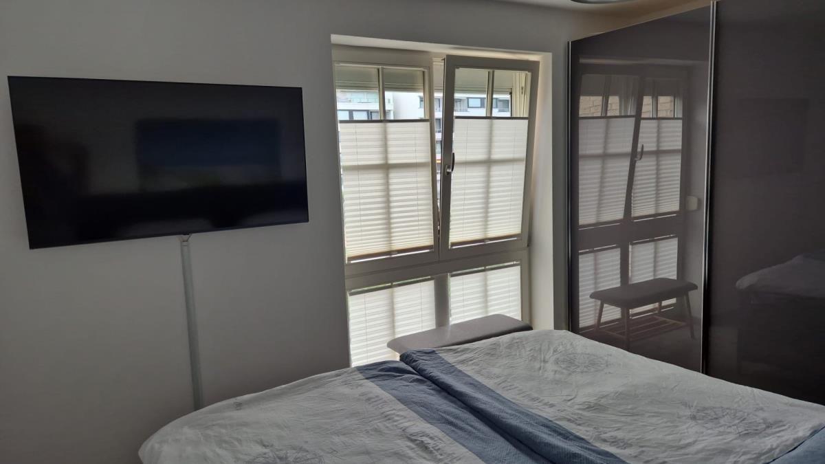 Schlafzimmer mit Bett, TV und Fenster mit Jalousien.