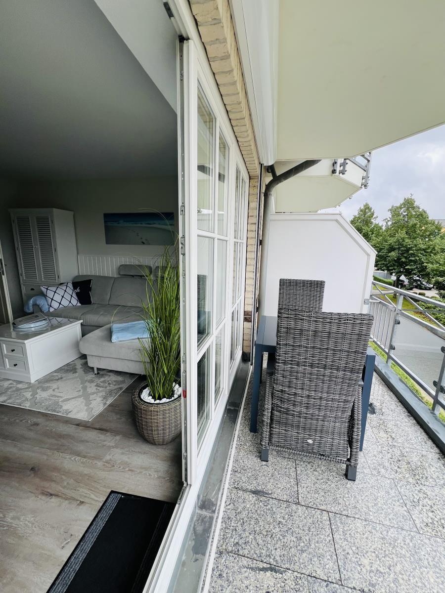 Terrasse mit Tisch und Stühlen. Blick ins Wohnzimmer mit Sofa und Pflanze.