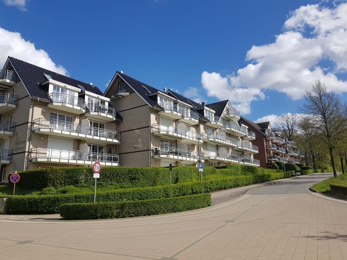 Reihenhaus mit Balkonen und begrünter Umgebung unter blauem Himmel.