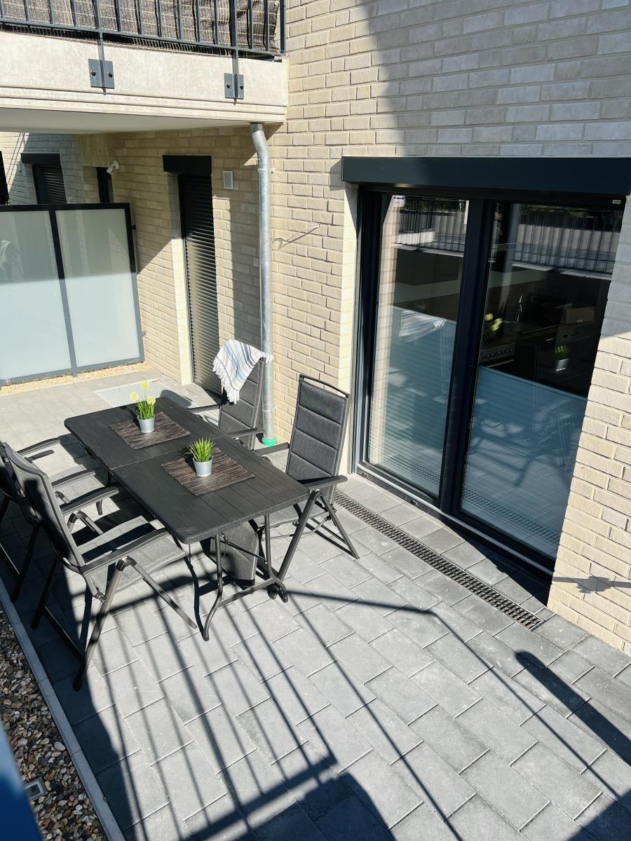 Terrace with table and chairs, plants, and glass sliding doors to the apartment.