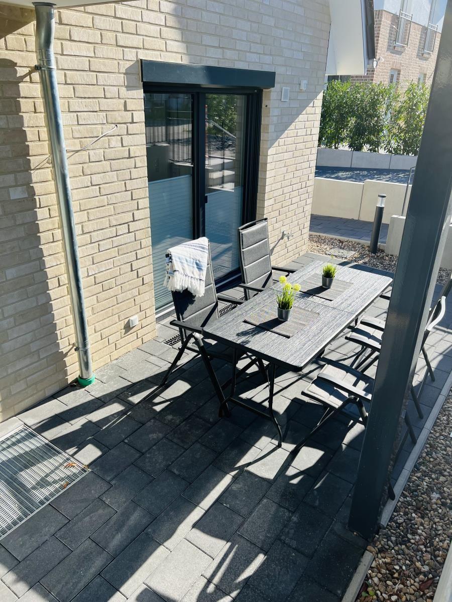 Terrace with table, chairs, and plants. Background: house wall and sliding door.