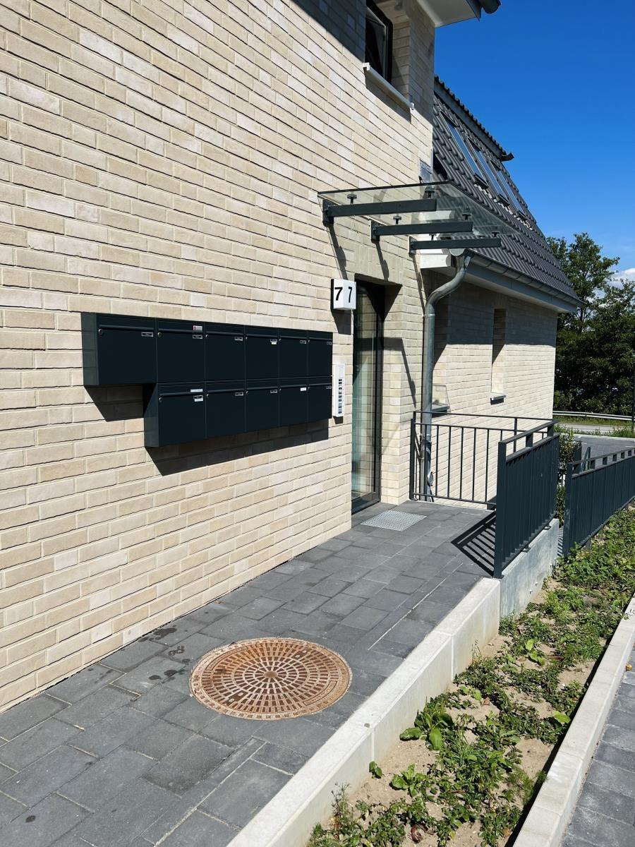 Entrance area with mailbox and house number 77 on a modern stone wall.