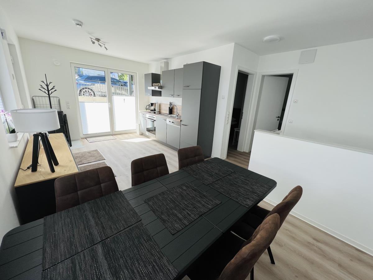 Dining area with table and chairs, kitchen, and terrace door in background.