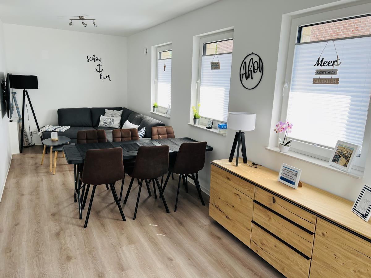 Living and dining area with sofa, table, chairs, windows with blinds, and wooden cabinet.