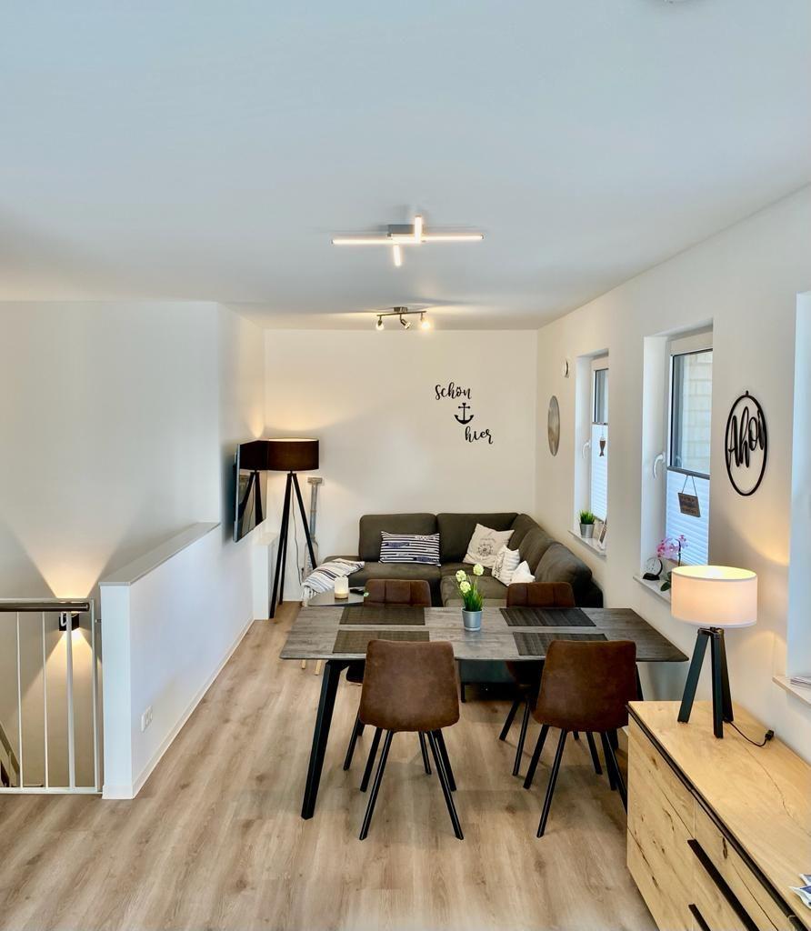 Living and dining area with sofa, table and chairs. Wooden floor and windows.