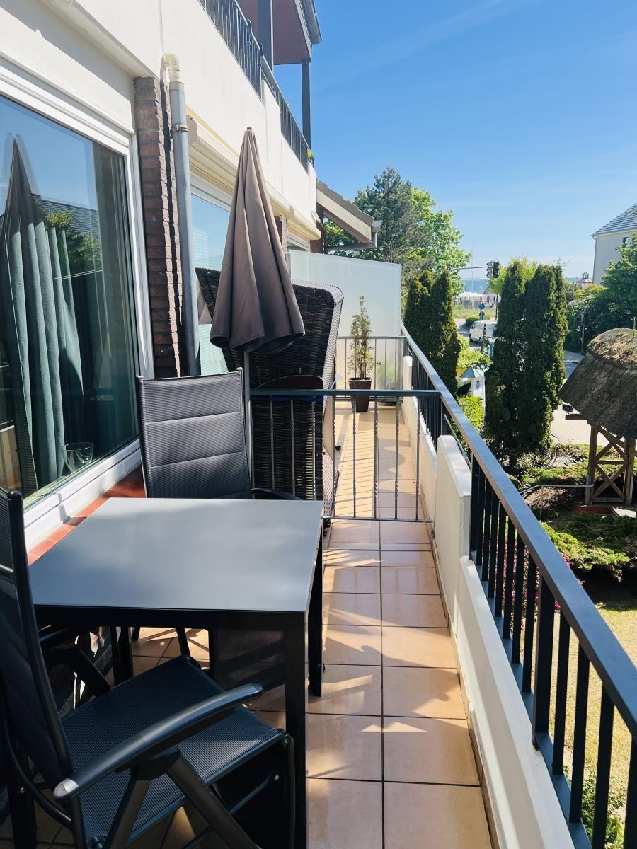 Terrasse mit Tisch, Stühlen und Sonnenschirm. Blick auf Garten und Straße.