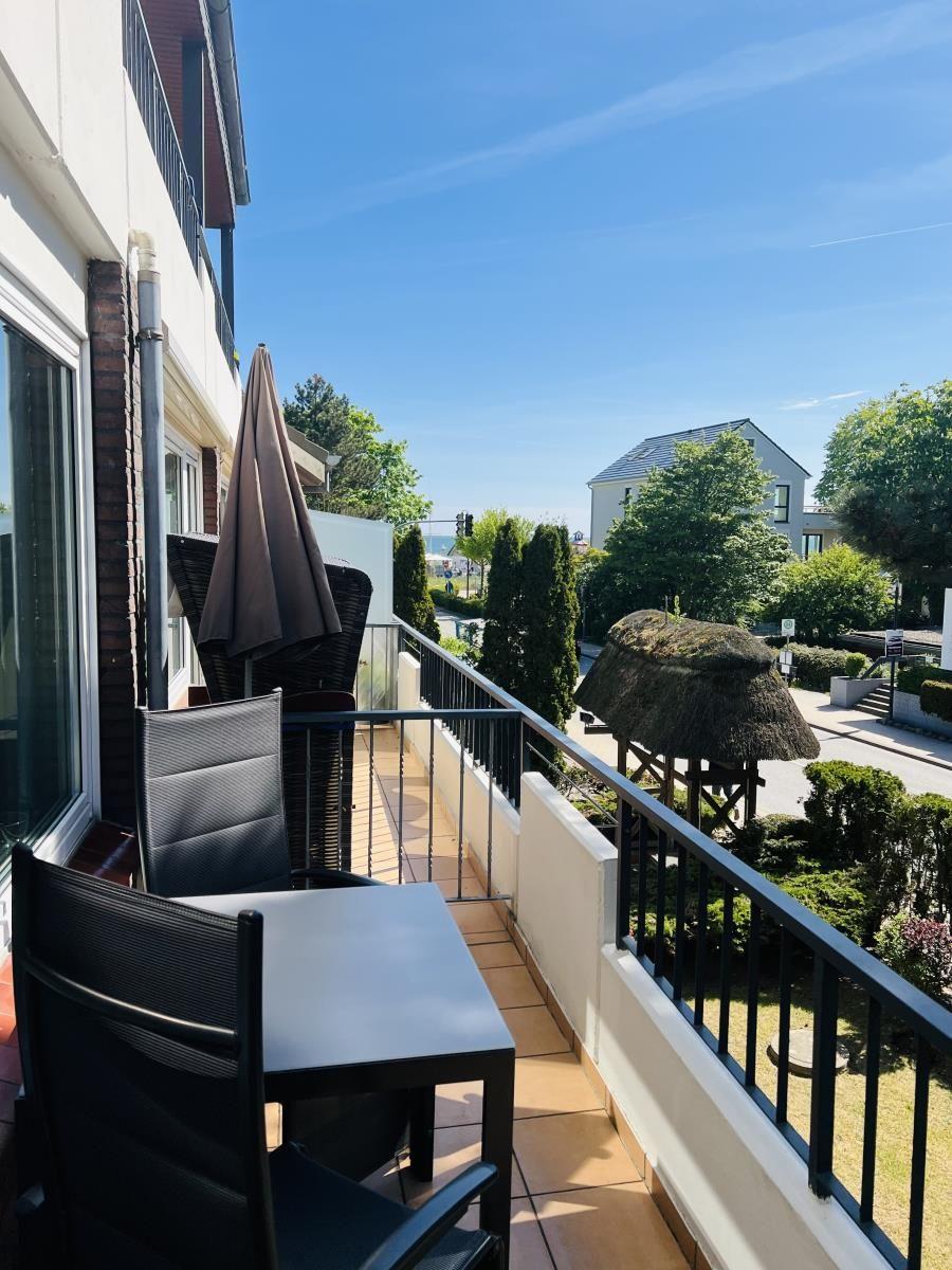 Terrasse mit Tisch, Stühlen und Sonnenschirm. Blick auf Garten und Straße.