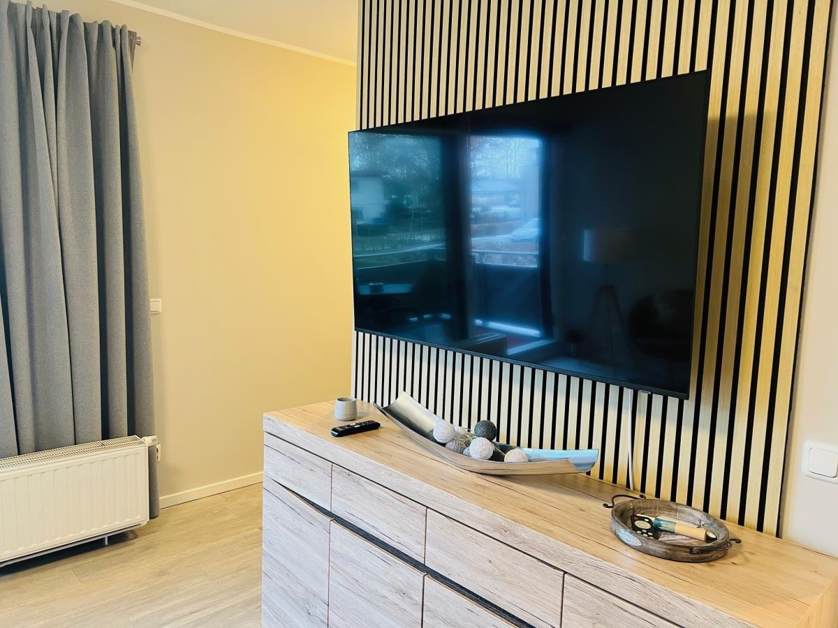 TV an Wand montiert, Holzkommode mit Dekoration und graue Vorhänge