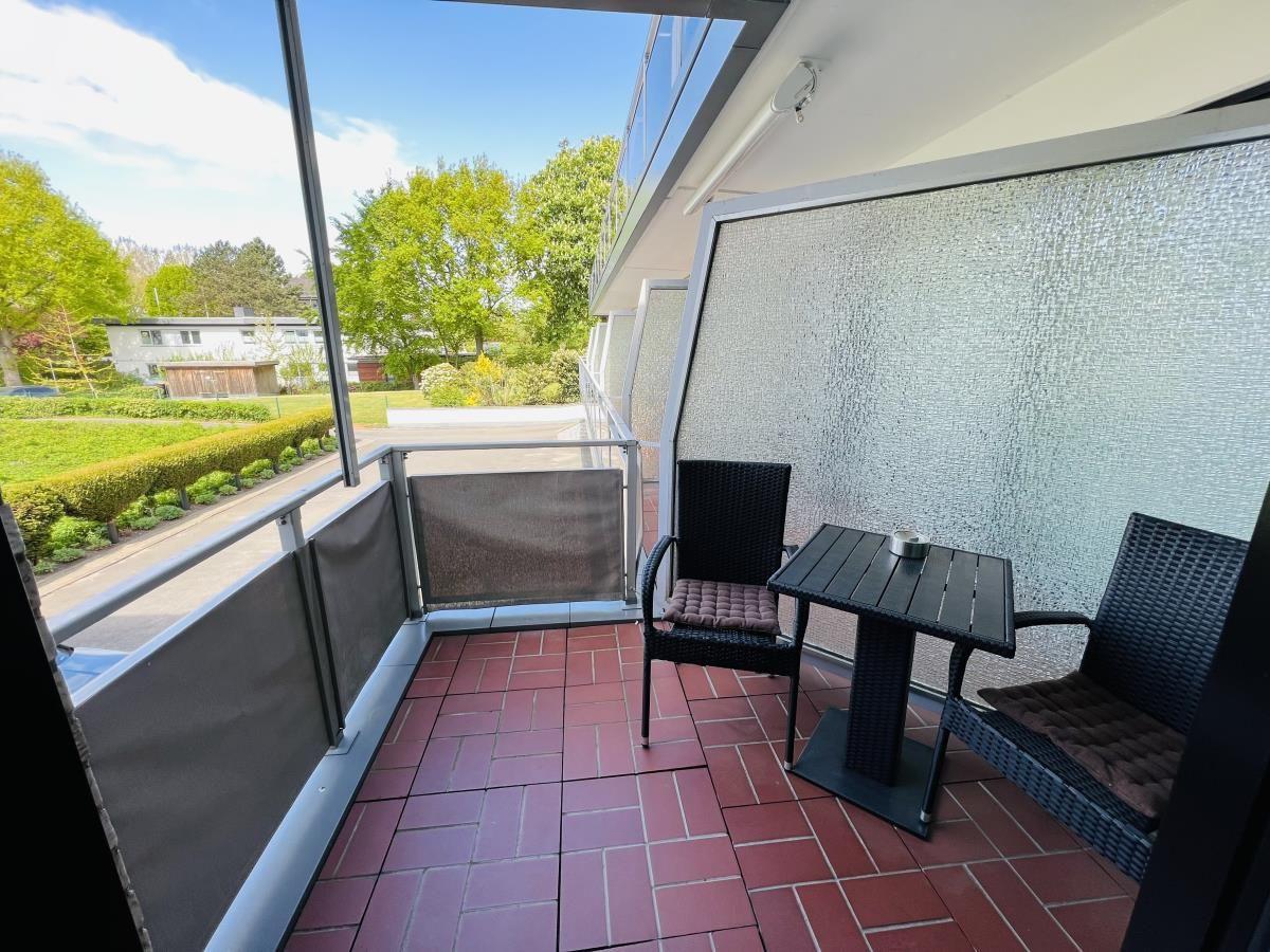 Terrasse mit Tisch und zwei Stühlen, Blick auf grüne Bäume und Rasenflächen.