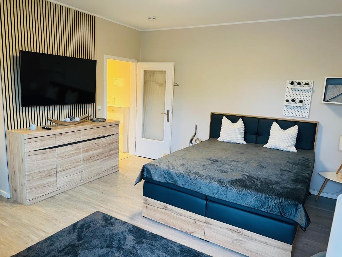 Schlafzimmer mit Bett, TV und Schrank. Tür führt in angrenzenden Raum.