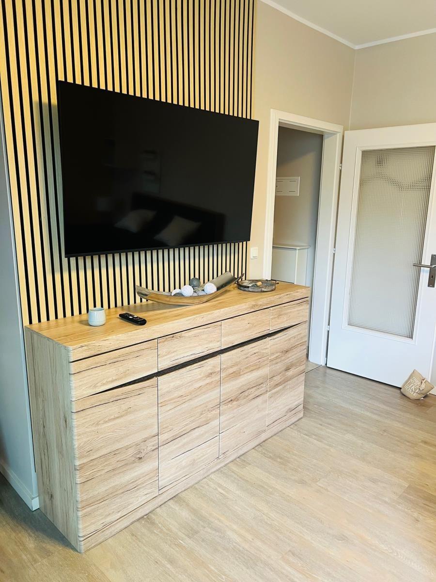 TV auf Holzwand, Sideboard mit Dekoration und Tür im Hintergrund.
