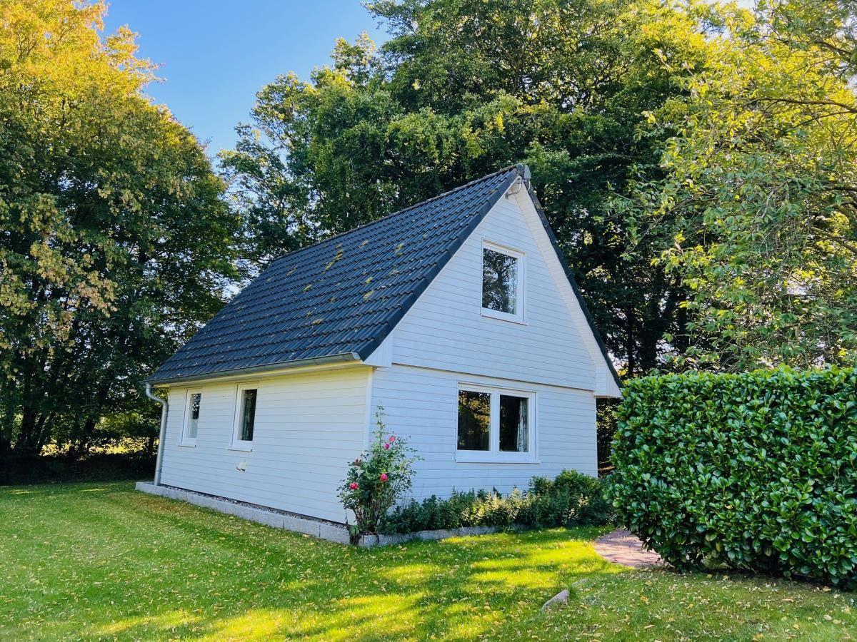 Weißes Haus mit dunklem Dach, umgeben von Gras und Bäumen.