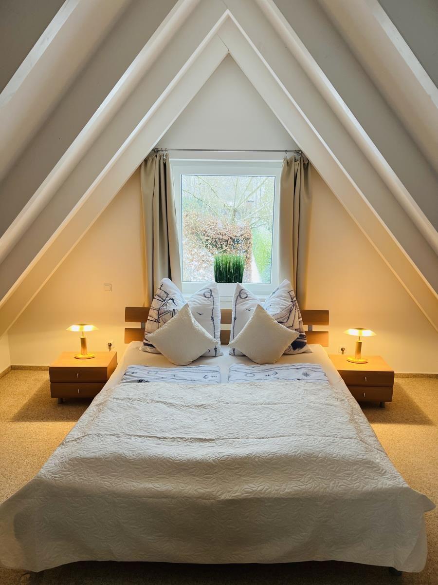 Schlafzimmer mit Dachschrägen, Bett, zwei Nachttischen und Fenster.