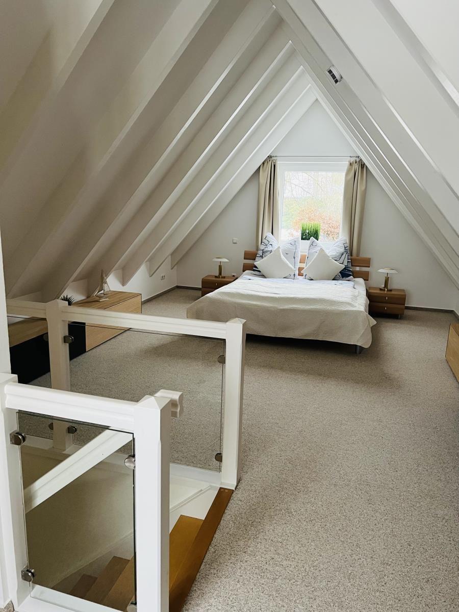 Schlafzimmer mit Dachschrägen, Bett, Nachttische und Fenster.