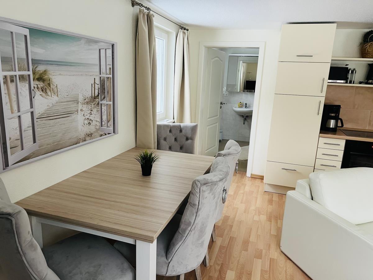 Essbereich mit Tisch, Stühlen und Küchenbereich. Wandbild zeigt Strand.