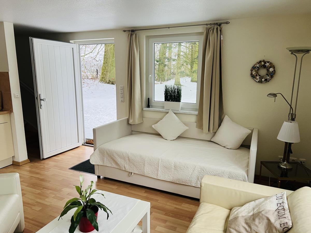 Wohnraum mit Schlafsofa, Fenster und Tür zum Garten.