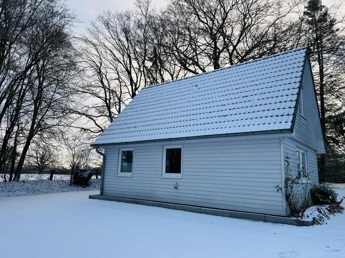 Wohnhaus mit schneebedecktem Dach und weißen Wänden in winterlicher Umgebung.