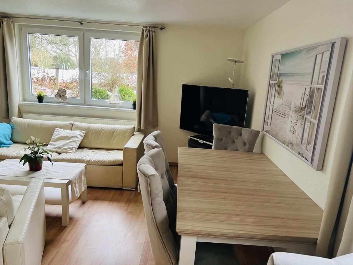 Wohn- und Essbereich mit Sofa, TV und Tisch. Fenster mit Blick auf Garten.