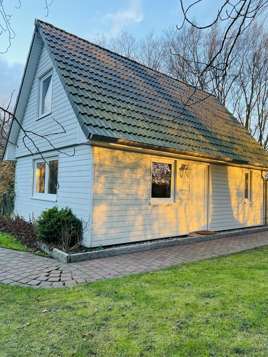 Haus mit hellen Wänden, schwarzem Dach und Vorgarten