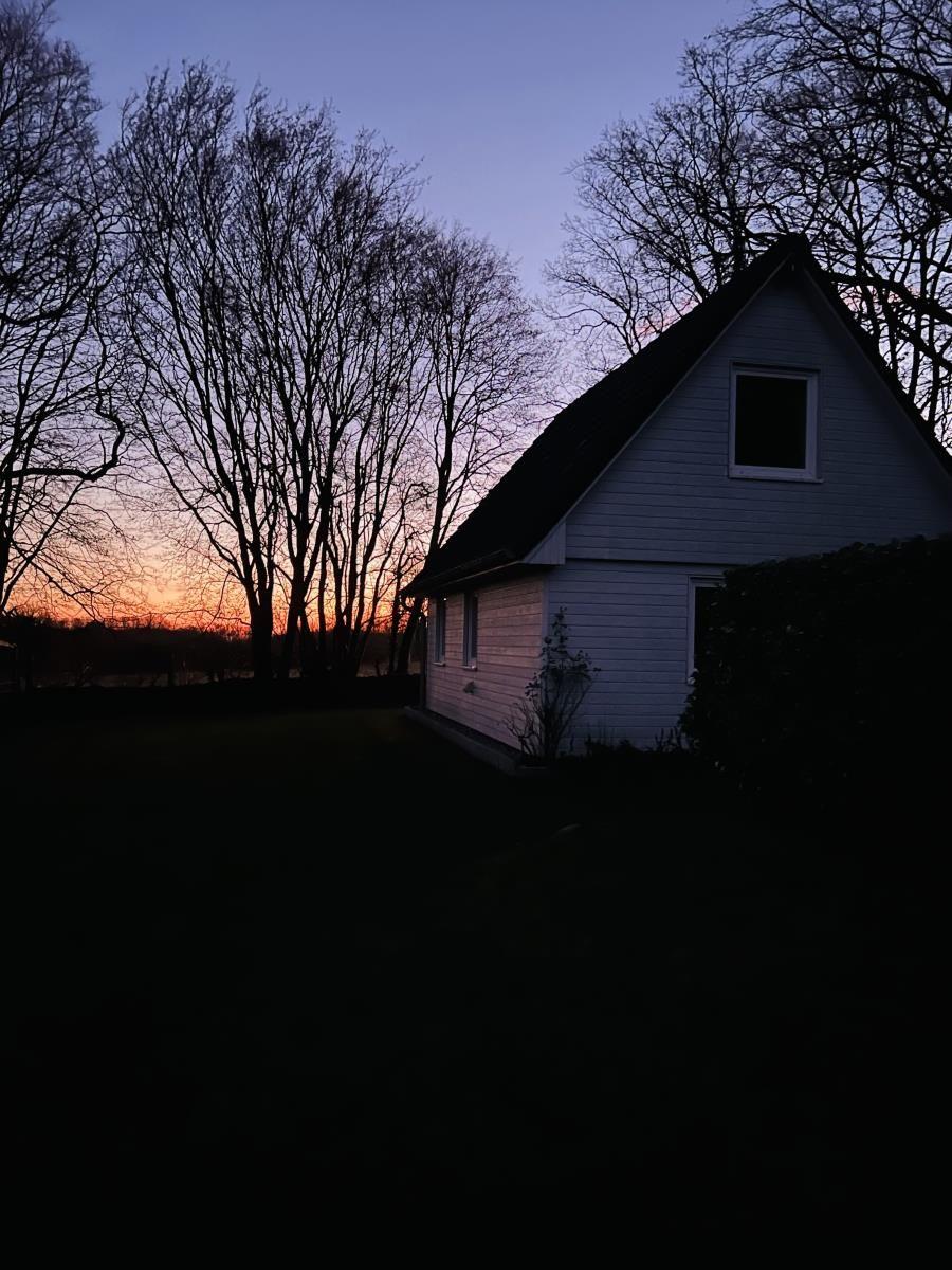 Haus mit Dach und Fenstern bei Sonnenuntergang hinter Bäumen.