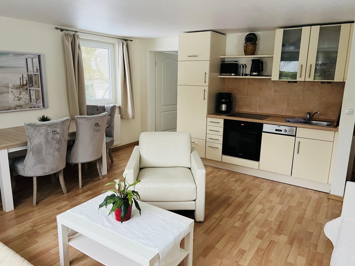 Wohnküche mit Essbereich, weiße Sitzgelegenheiten und Holzboden.