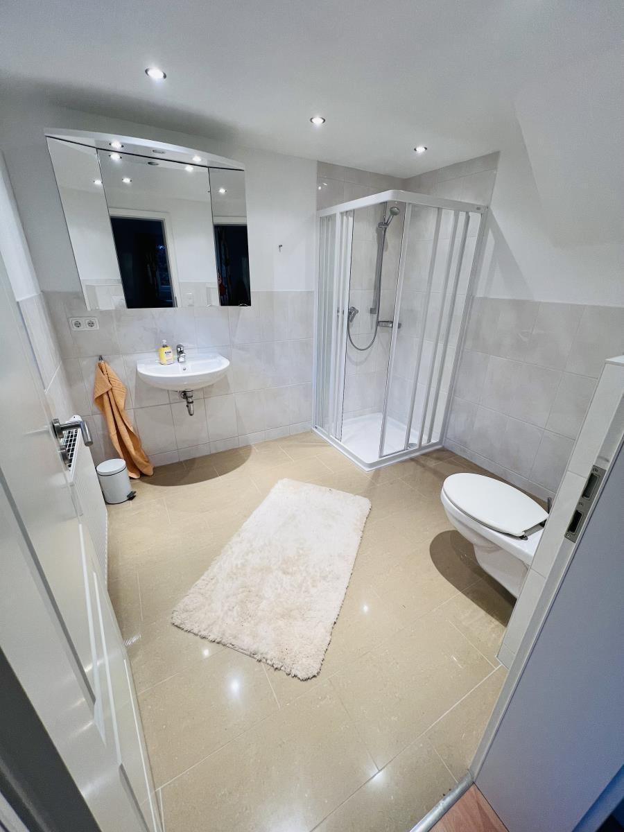 Badezimmer mit Dusche, Waschbecken und Toilette. Fliesenboden und Spiegel.