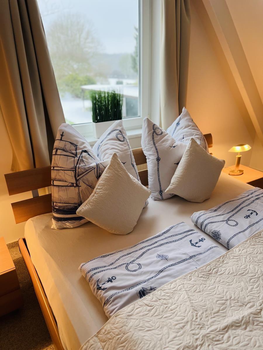 Schlafzimmer mit Bett, Kissen und Fenster. Möbel sind hölzern.
