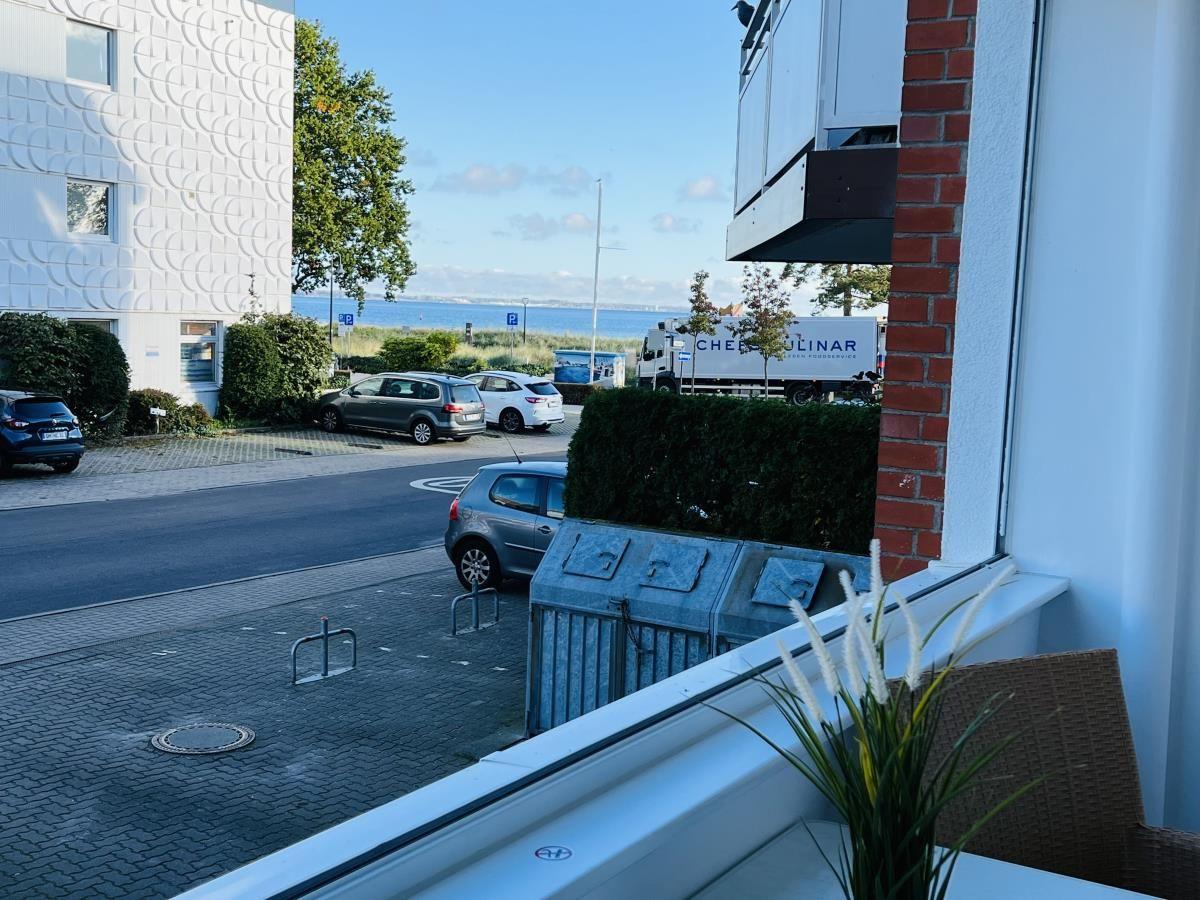 Blick vom Balkon auf Straße, Parkplatz und Hafen mit Booten.