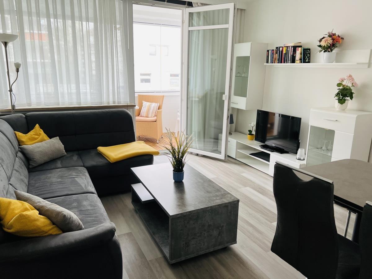 Wohnzimmer mit Sofa, Couchtisch und TV. Balkon mit Sitzgelegenheit.