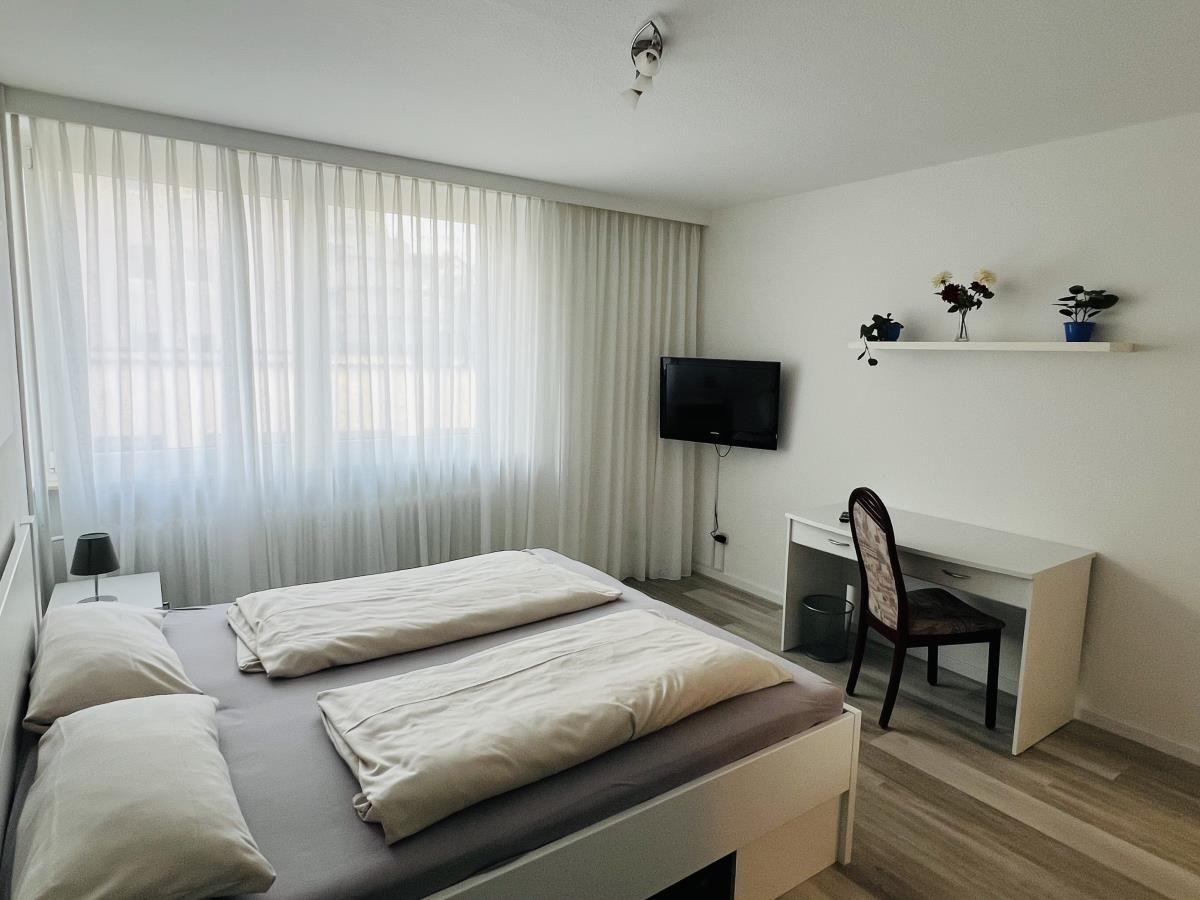 Schlafzimmer mit Doppelbett, Schreibtisch und TV an der Wand.