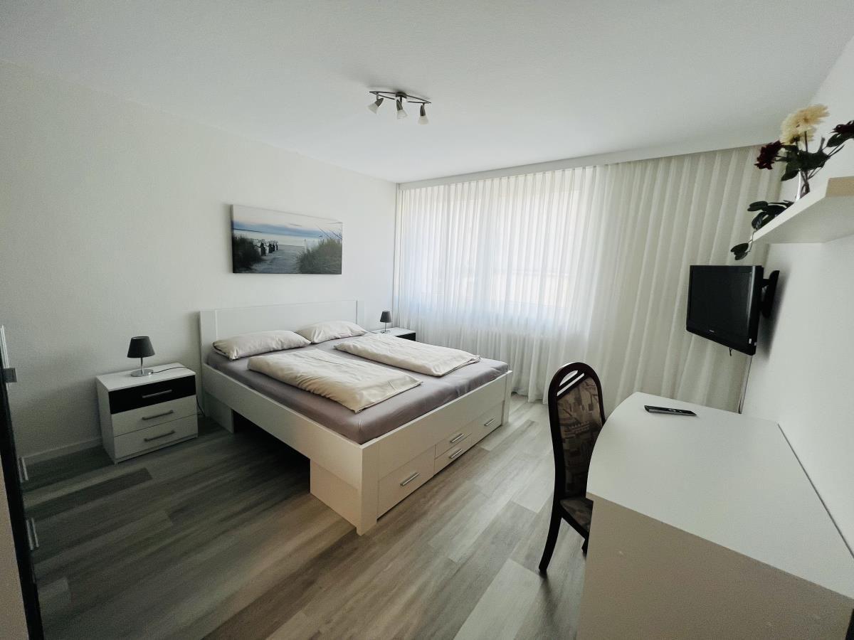 Schlafzimmer mit Bett, Schreibtisch und Fernseher an der Wand.