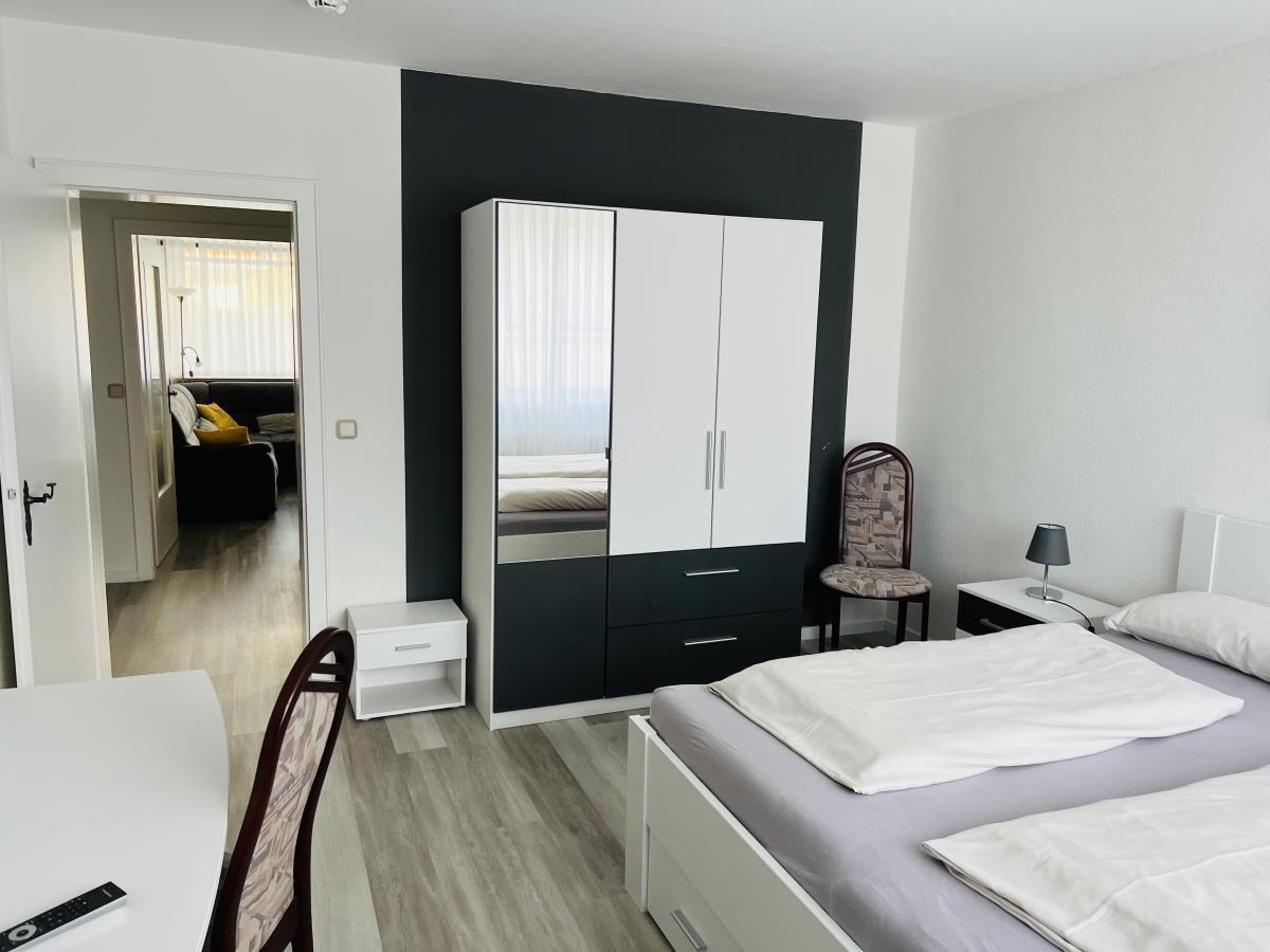 Schlafzimmer mit Bett, Kleiderschrank und Sicht auf Wohnzimmer.