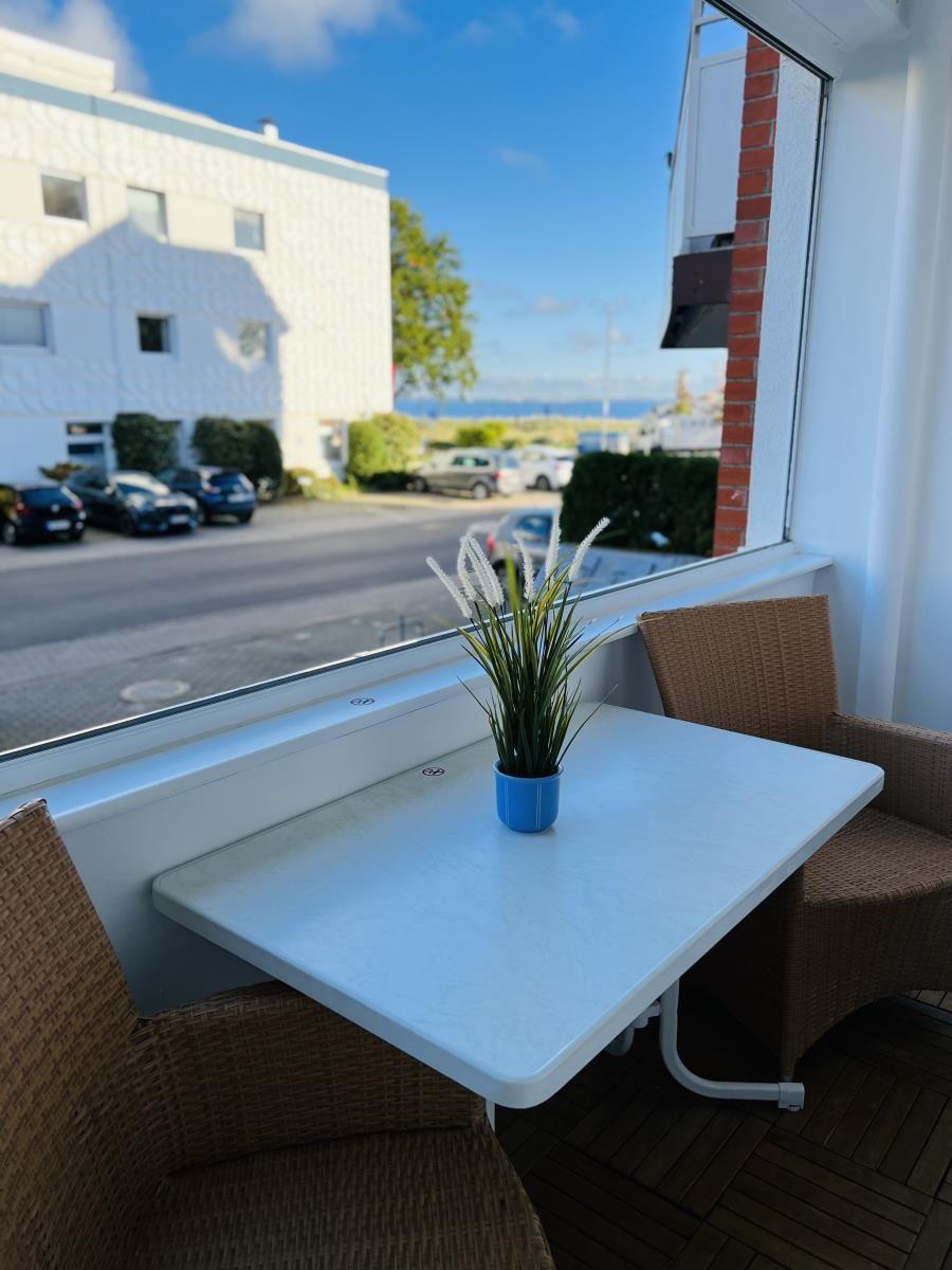 Balkon mit Tisch und zwei Stühlen, Blick auf Straße und Wasser.