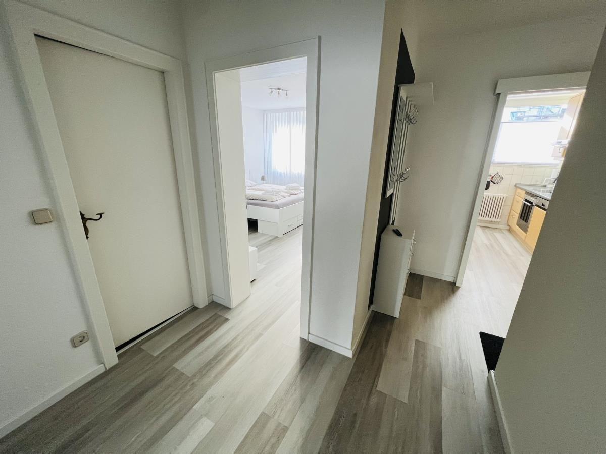 Flur mit Blick in Schlafzimmer und Küche. Holzboden und weiße Wände.