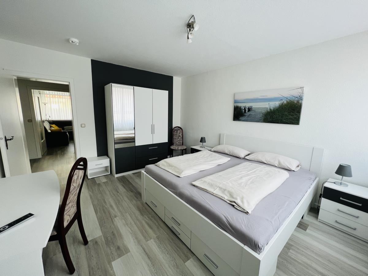 Schlafzimmer mit Doppelbett, Kleiderschrank und Tisch. Blick in Wohnbereich.