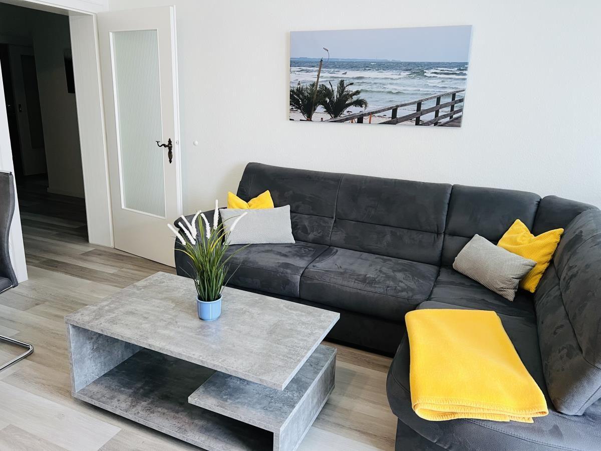 Wohnzimmer mit grauem Sofa, gelben Kissen und einem Tisch mit Pflanze.