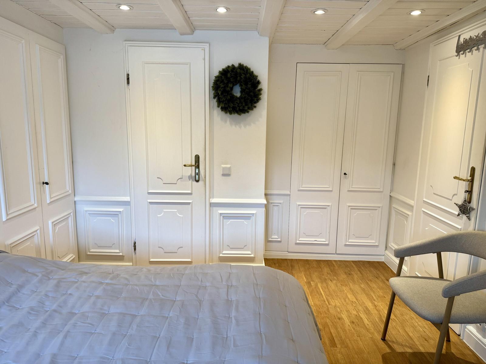 Schlafzimmer mit Bett, Stuhl und weißen Türen an den Wänden.