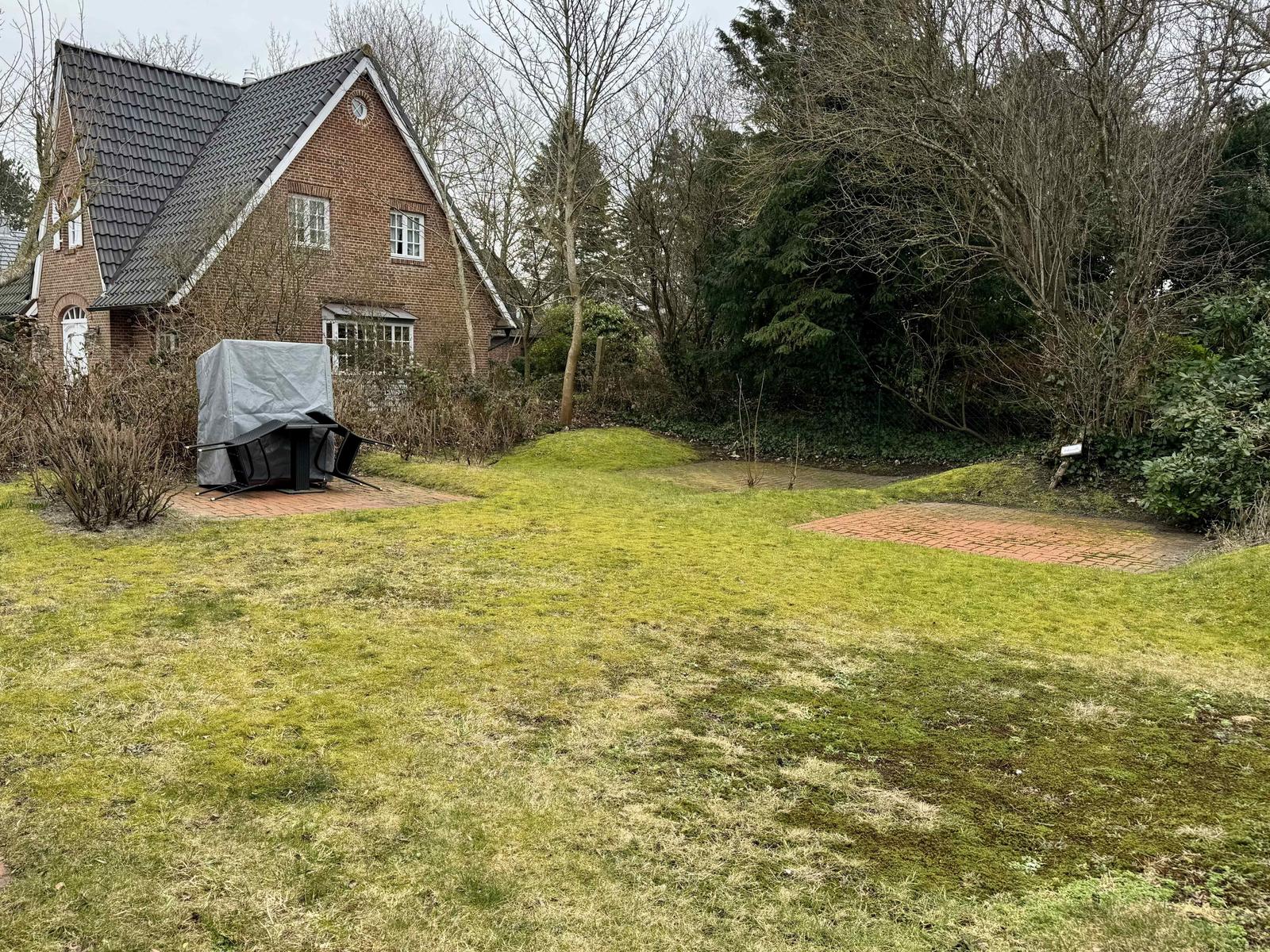 Haus mit Garten, Grillplatz und Bäumen im Hintergrund.