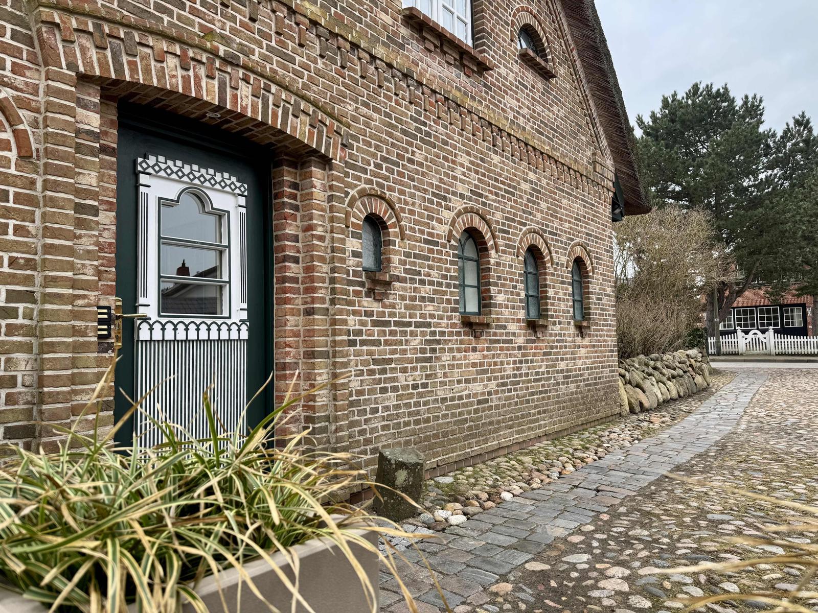 Haus mit Backsteinfassade, grüner Tür und Kiesweg. 