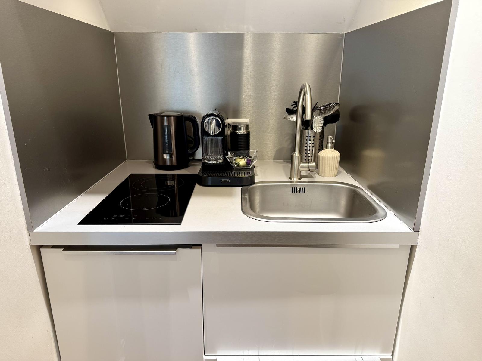 Küchenbereich mit Spüle, Induktionskochfeld und Kaffeemaschine.
