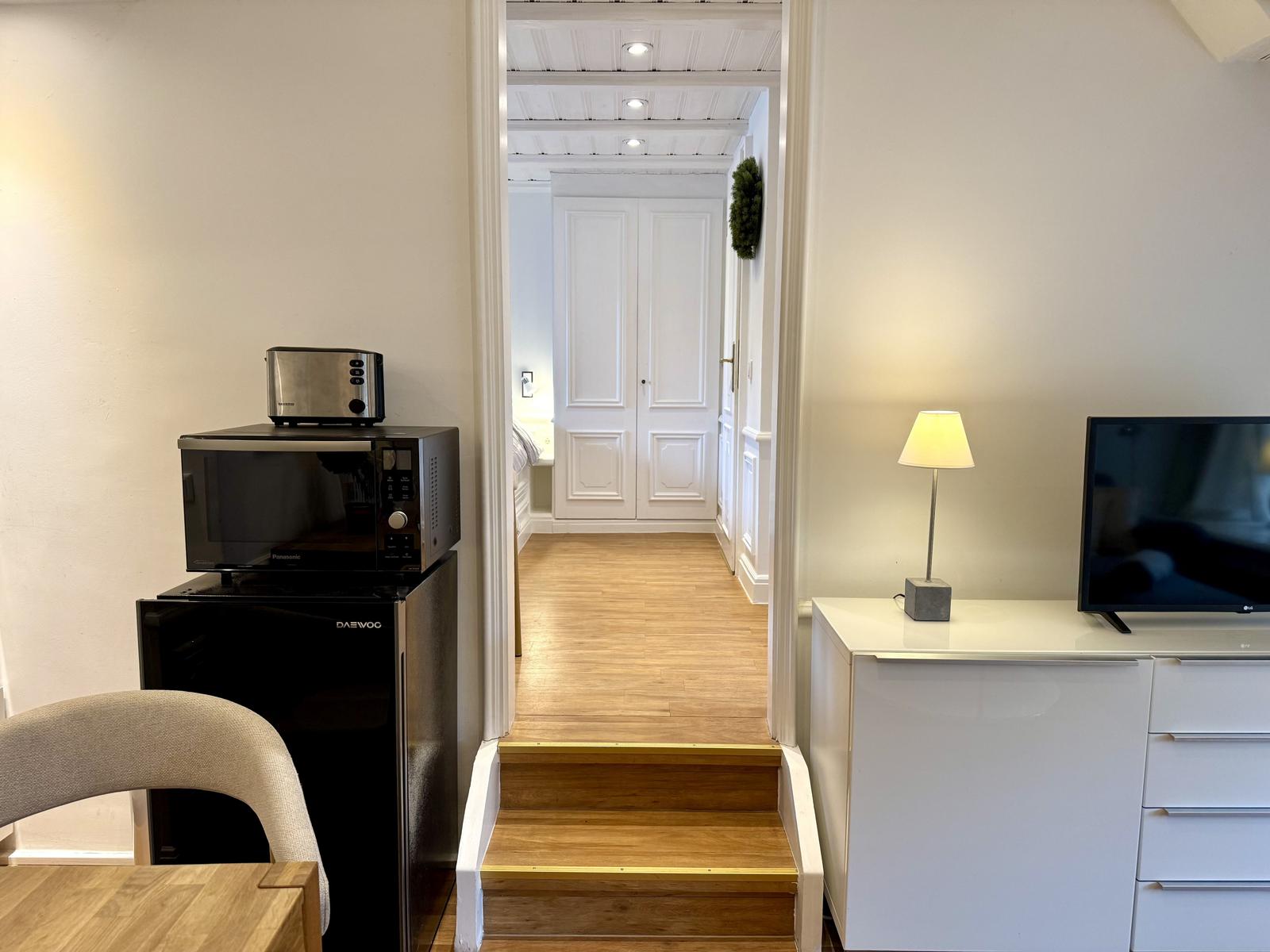 Küche mit Kühlschrank und Mikrowelle. Treppenhaus führt zu Schlafzimmer.