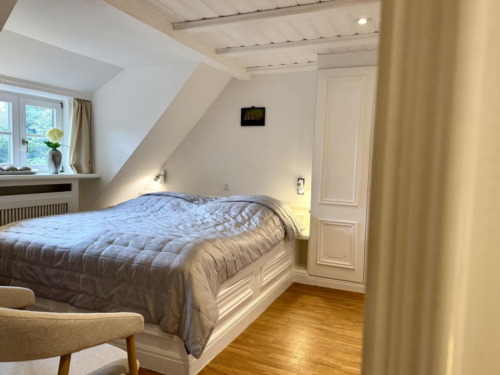 Schlafzimmer mit Dachschrägen, Bett, Fenster und Holzboden.