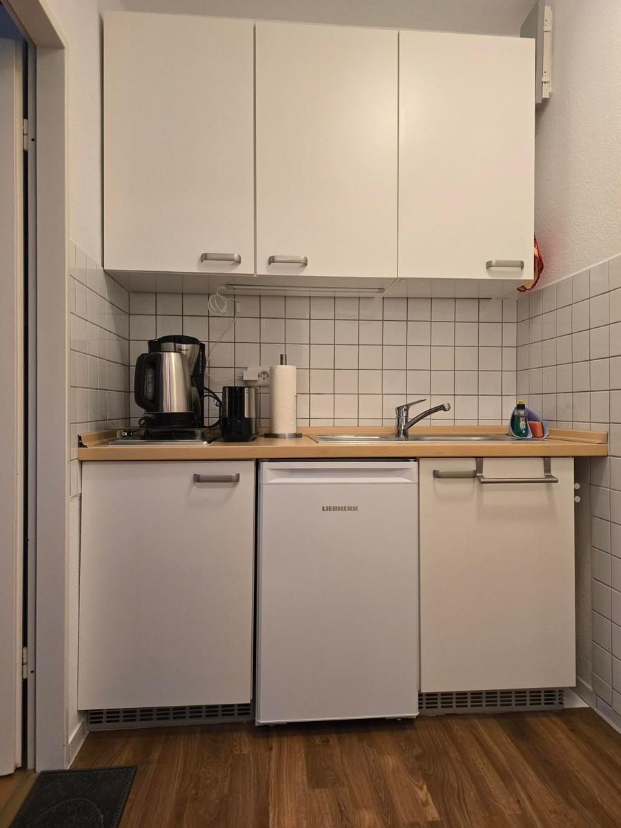 Küche mit weißen Schränken, Spüle und Kühlschrank.