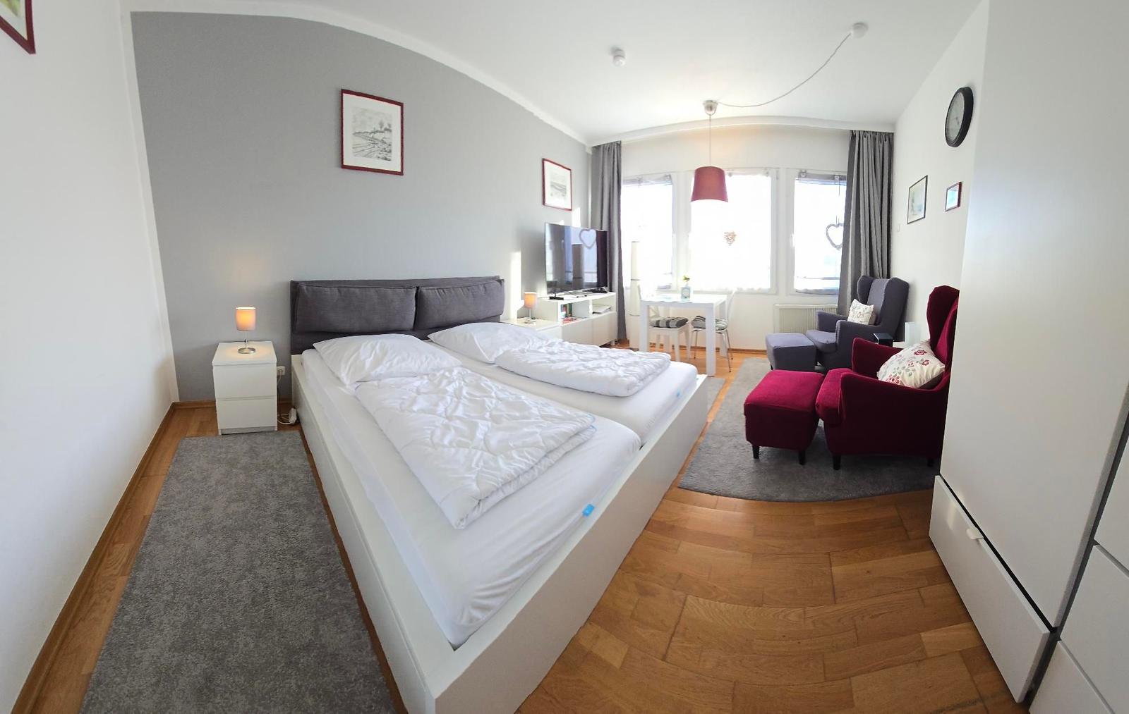 Schlafzimmer mit Doppelbett, Wohnbereich mit rotem Sessel und TV.