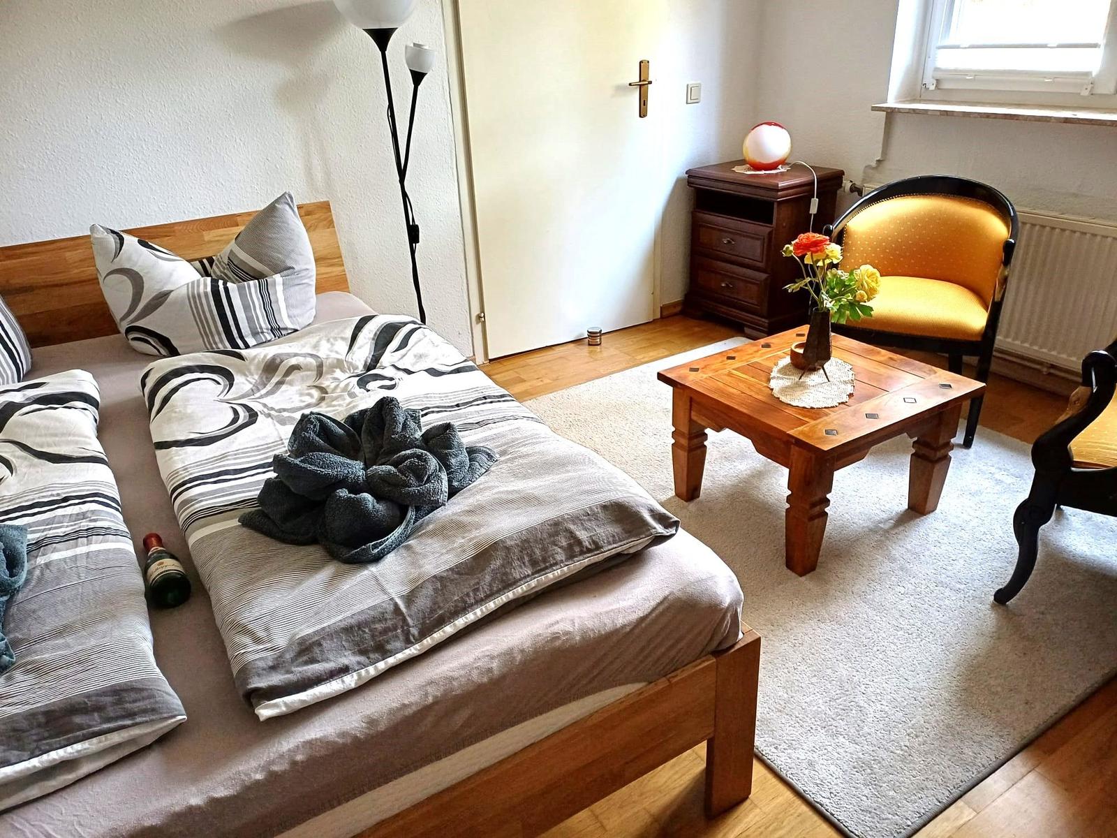 Ein Schlafzimmer mit Bett, Stuhl, Tisch und Fenster.