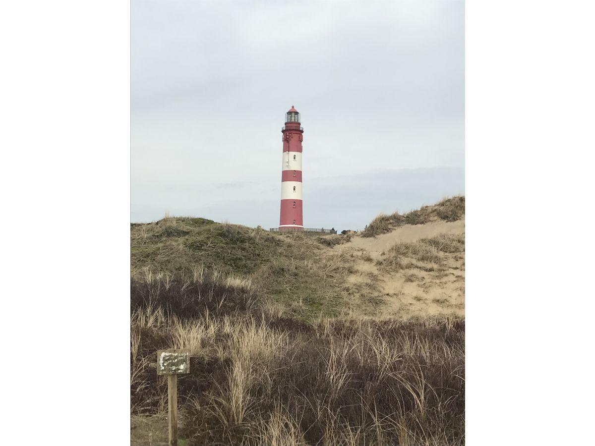 Roter Leuchtturm mit weißer Strebe auf Dünen im Hintergrund.