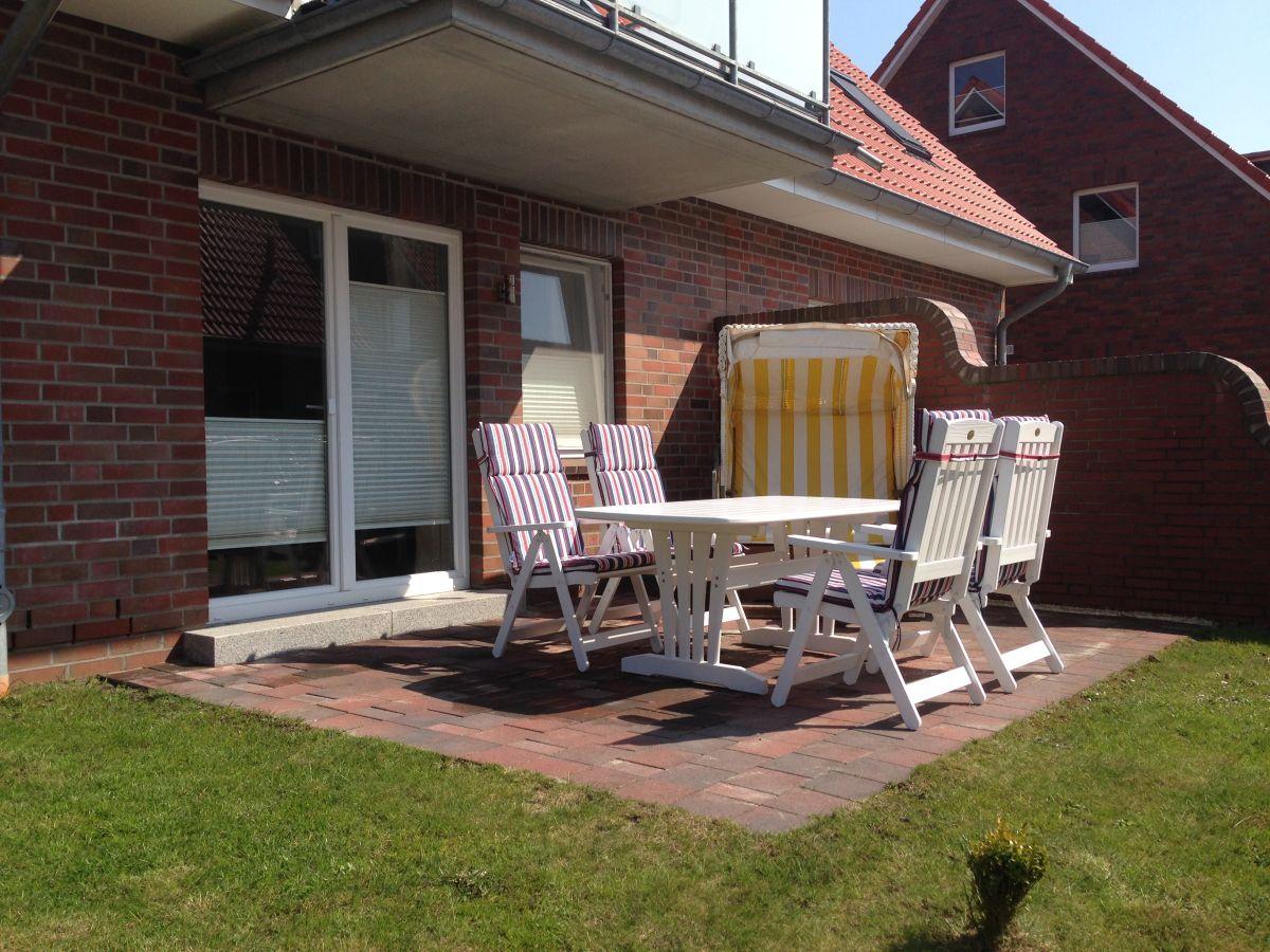 Terrasse mit weißem Tisch, Stühlen und Sonnenschirm. Hintergrund: roter Backsteinbau mit Fenstern.